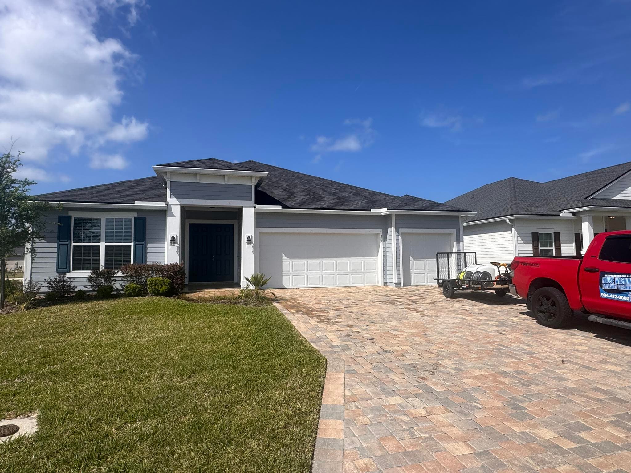 Single-story grey home with a brick paver driveway and a red pressure washing truck parked.