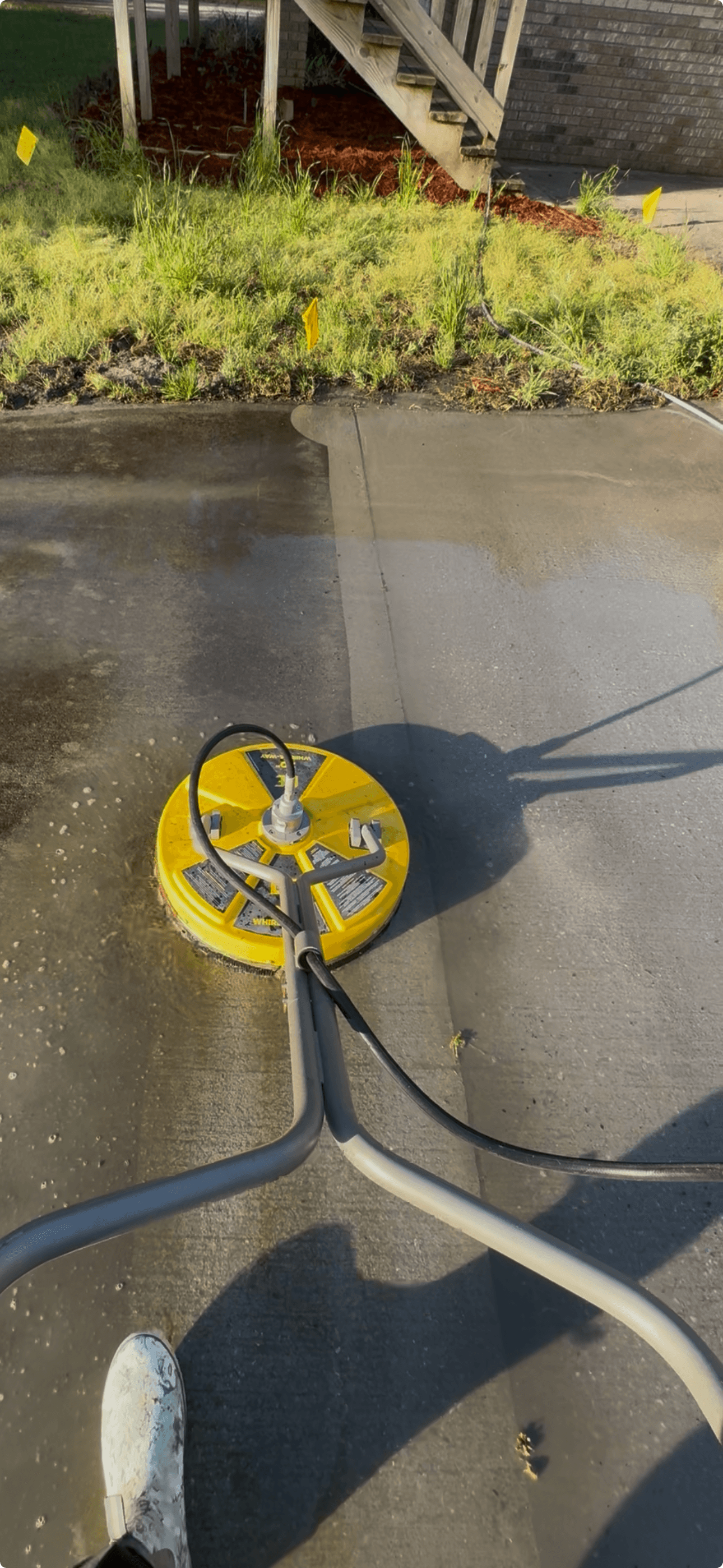 Yellow surface cleaner pressure washing a driveway, showing a clear contrast between dirty and clean.