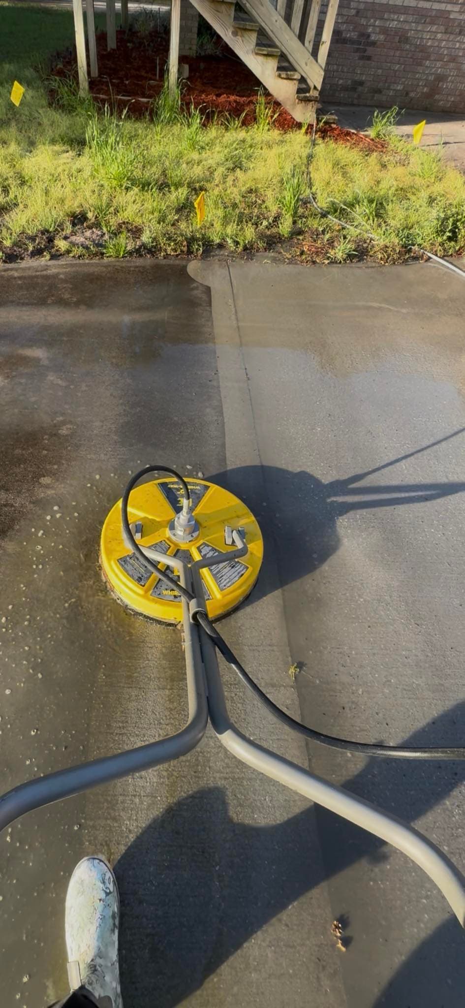 Yellow surface cleaner pressure washing a concrete driveway, revealing a clean surface beneath the dirt.