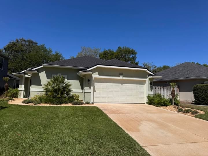 Single-story sage green home with a white garage door and a concrete driveway.