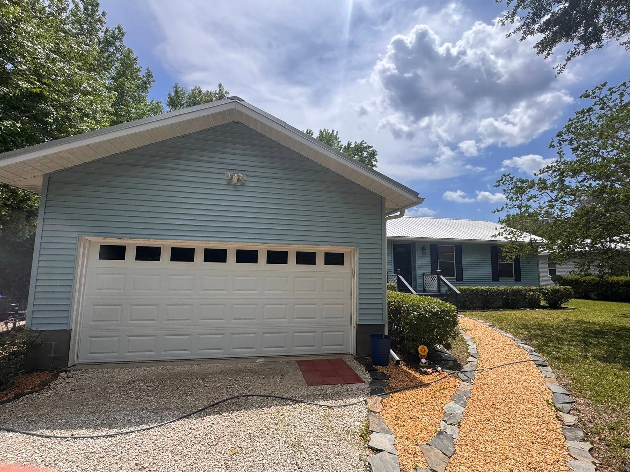Light blue house featuring a white garage door and a stone-edged orange pebble garden path.