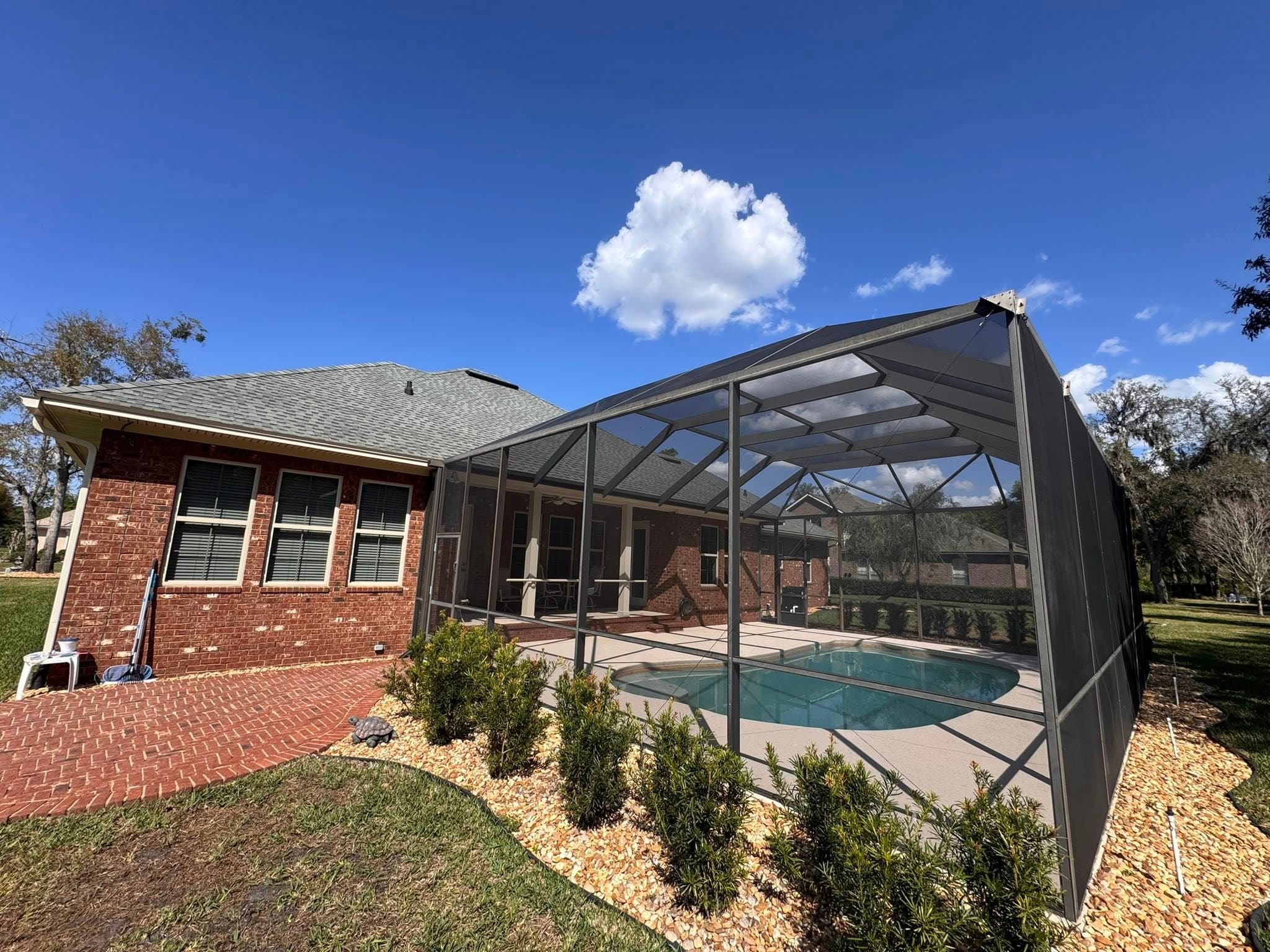 Red brick house with a screened-in swimming pool enclosure under a bright blue sky.